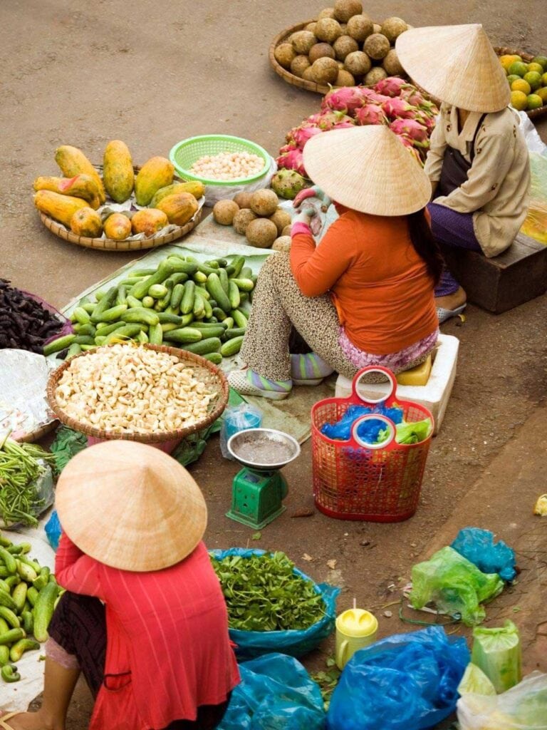 Three Vietnamese ladies sitting down selling fruit and vegetables. image for guide on things to know before traveling to Vietnam