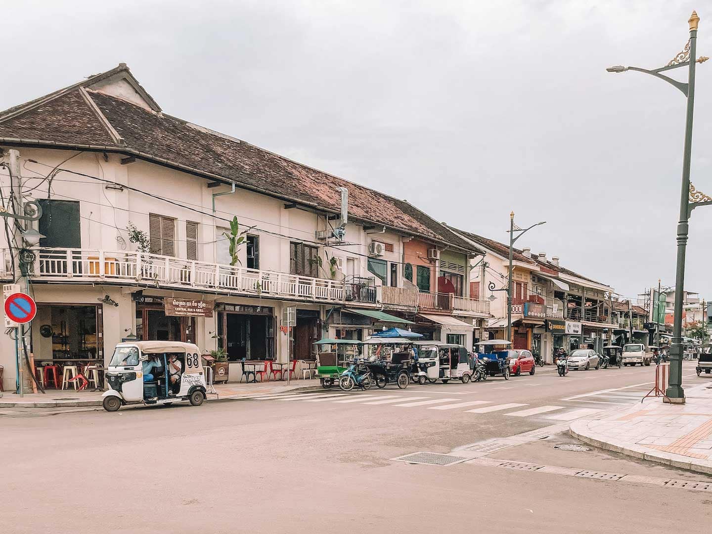 A street in Siem Reap city center on a cloudy day. There isn't much traffic but tuk tuks parked on the side of the road