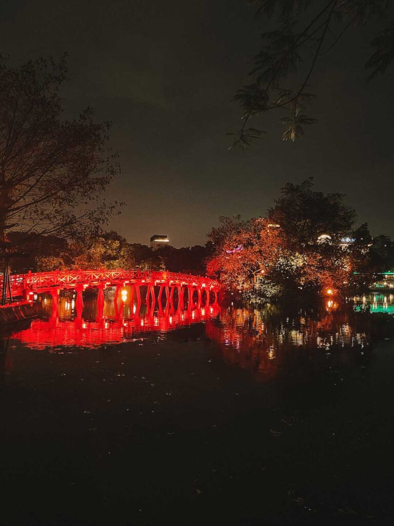 A photo taken at night of Hoan Kiem Lake in Hanoi and the bridge going over to Ngoc Son Temple is lite up in bright red