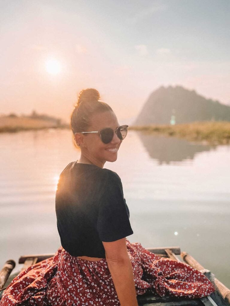 Elyse sitting on the edge of a bamboo boat in Vietnam during sunset. This is a A recommend day trip during one week in Hanoi.