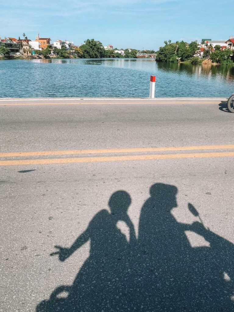 Our shadows on the road as we ride a scooter through Hue City centre