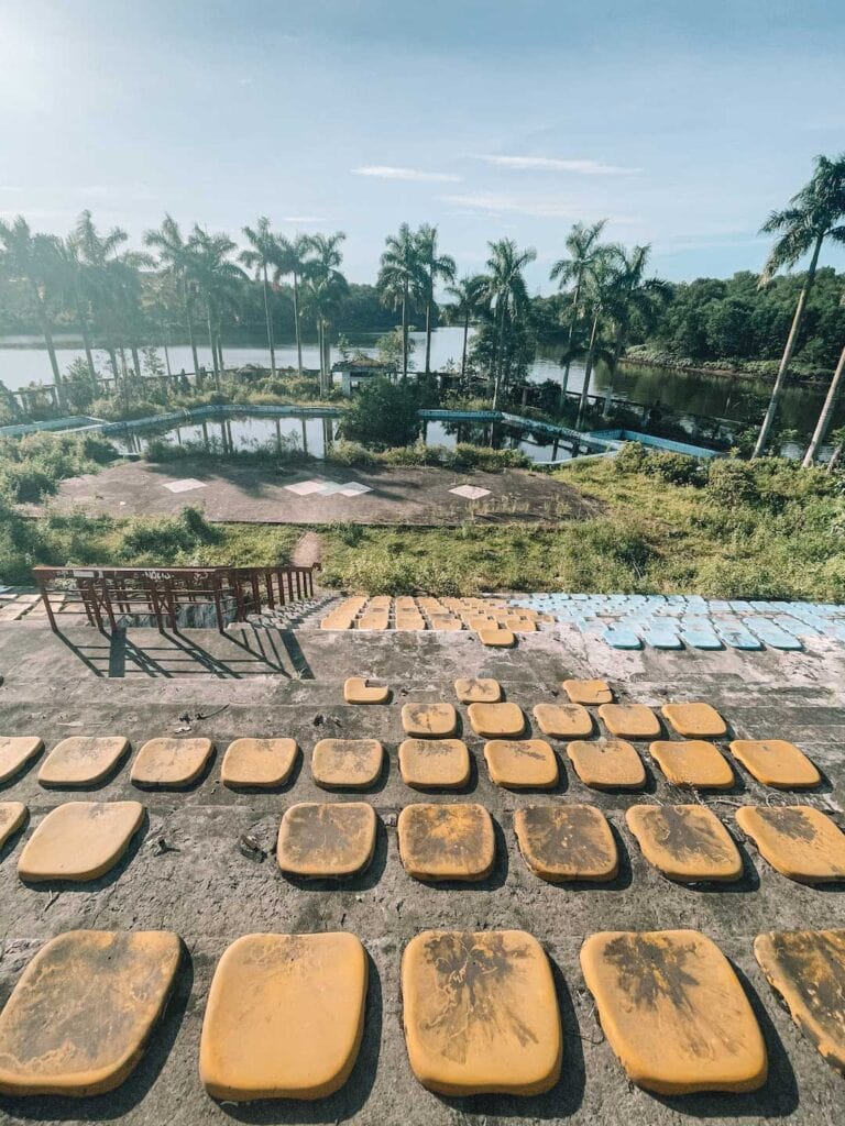 the stadium at the Thuy Tien Lake Abandoned Water Park. the yellow and blue seats are now dirty and the stadium over looks a large pond