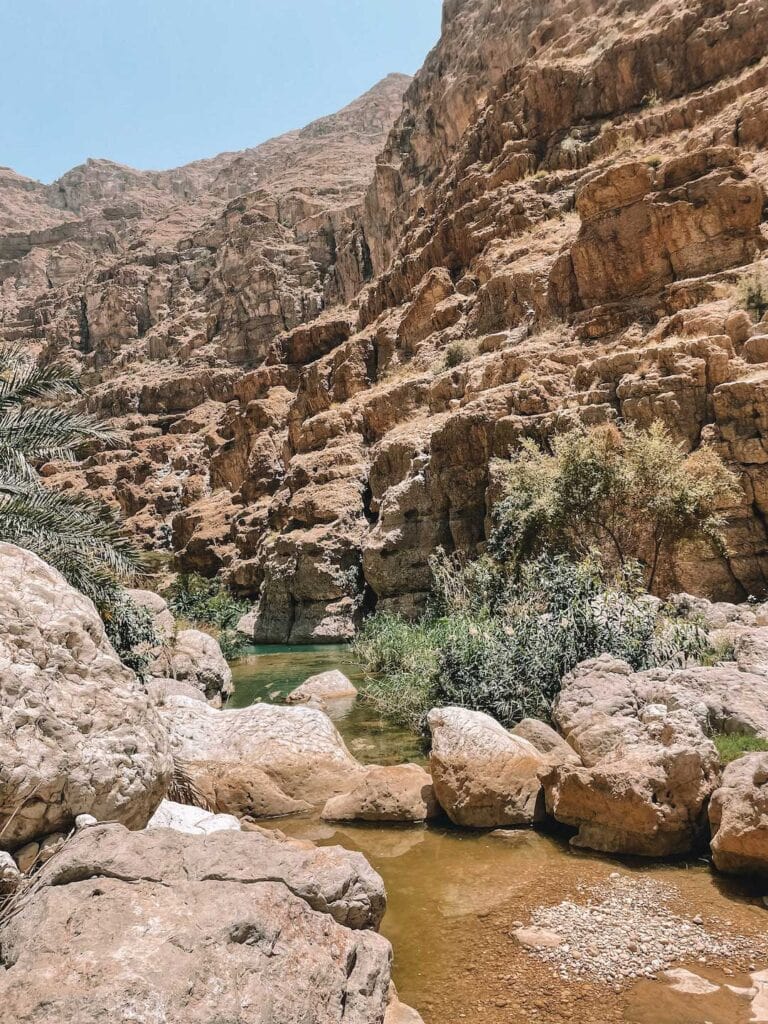 hiking the wadi shab in Oman, rugged cliffs surrounding the clear water