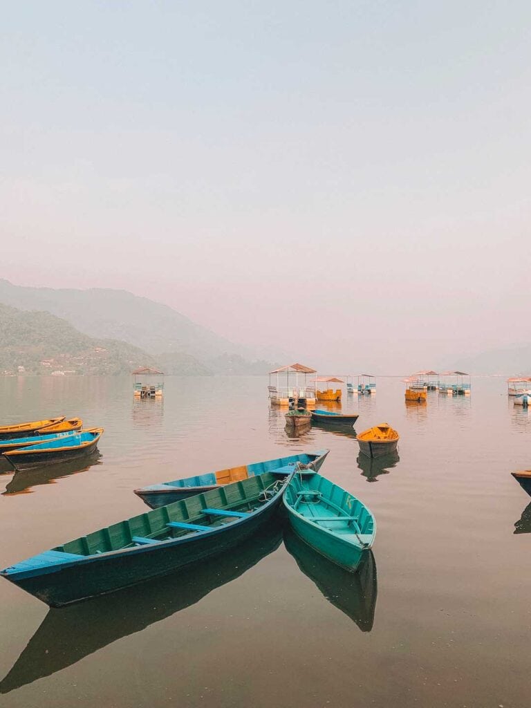 Phewa Lake in Pokhara on a misty day. Colorful row boats are anchored