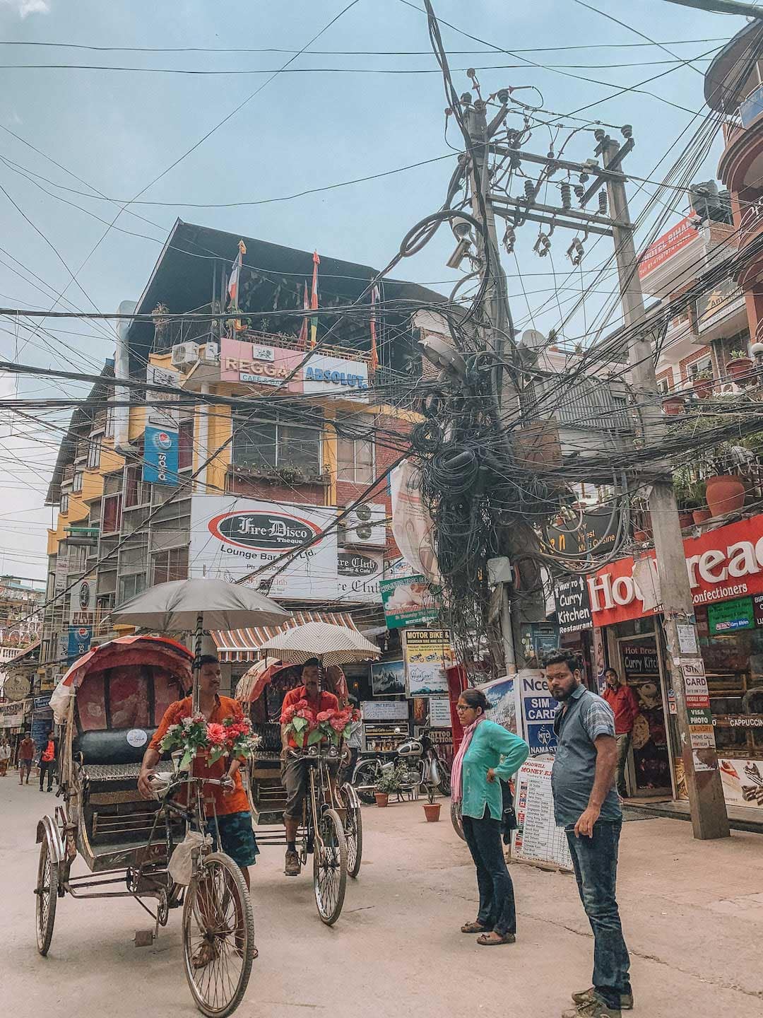 Busy street with a large knot of electrical wires. Two men on rickshaws on the road. Kathmandu Travel Guide