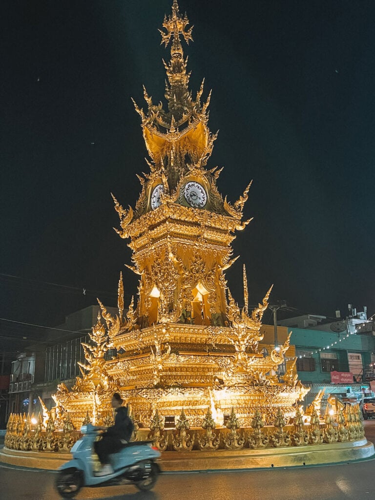 a motor bike riding past the Chiang Rai clocktower at night time