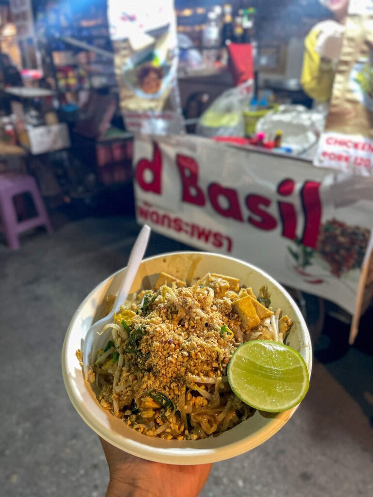 holding a bowl of pad Thai in Thailand, made along Pai walking street. things to do in Pai