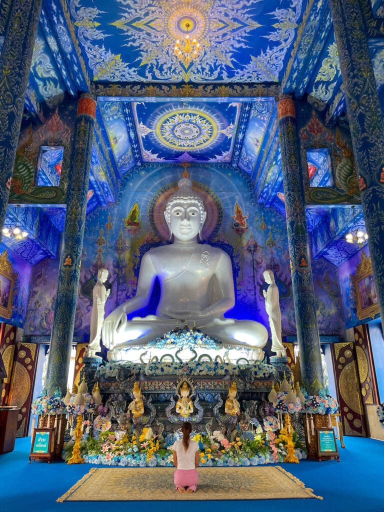 sitting in front of Buddha inside the main hall at the Blue Temple in Chiang Rai