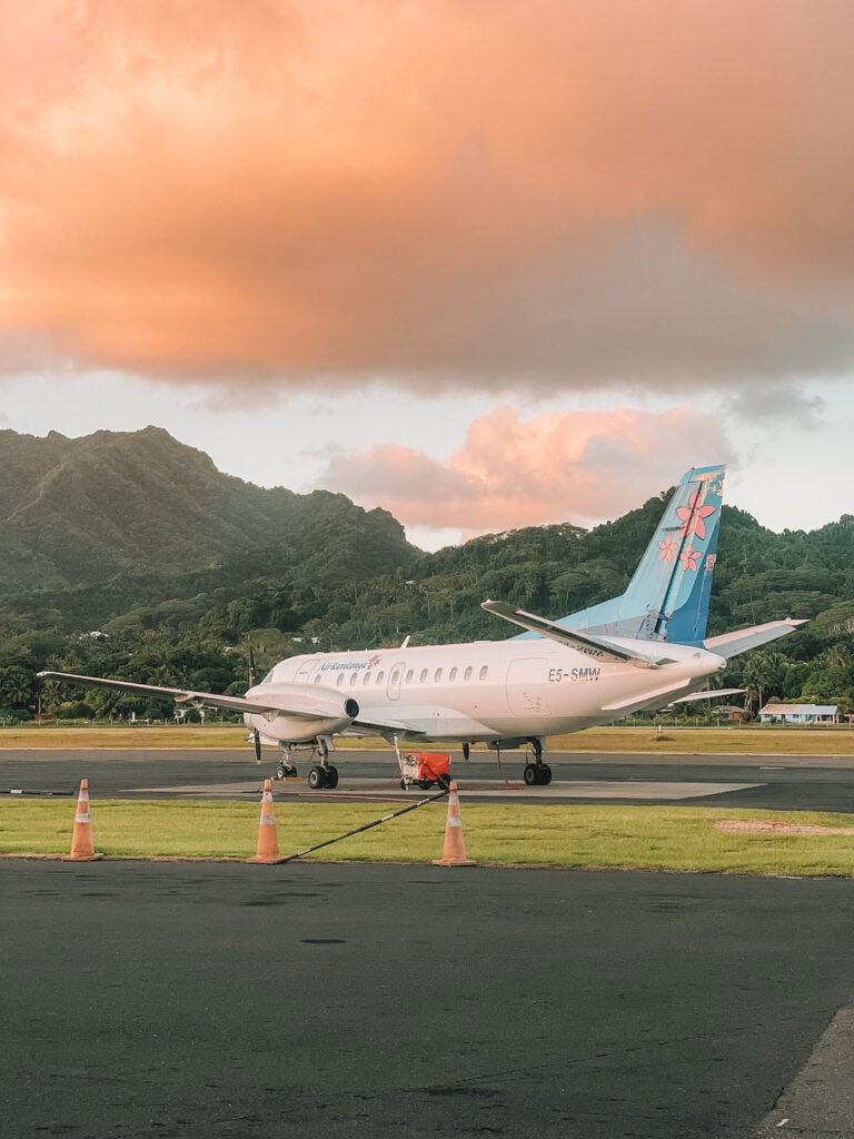 Small Air Rarotonga airplane parked on runway with scenic mountain background.