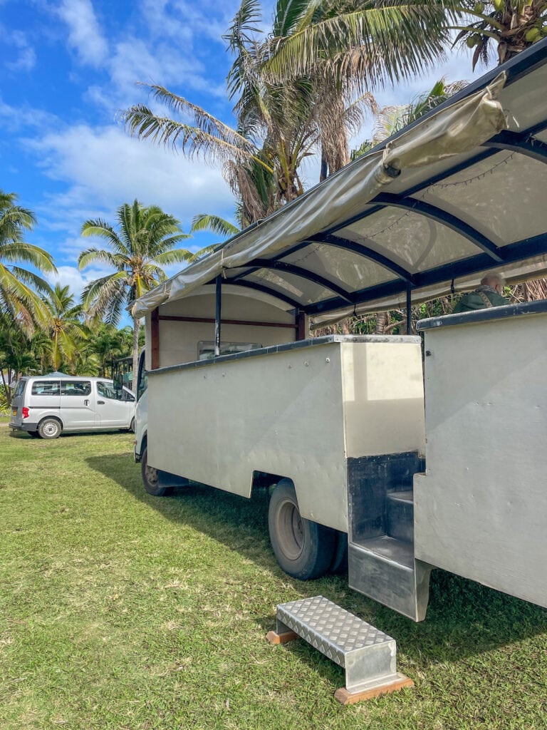 truck in a tropical setting with palm trees and blue sky, used as transportation during Aitutaki mainland tour