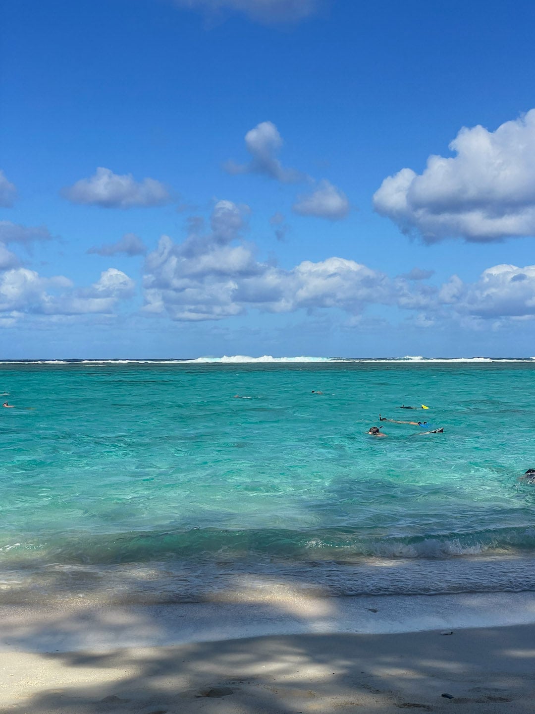 Turquoise ocean with swimmers and blue sky with clouds, snorkeling at Aroa marine reserve