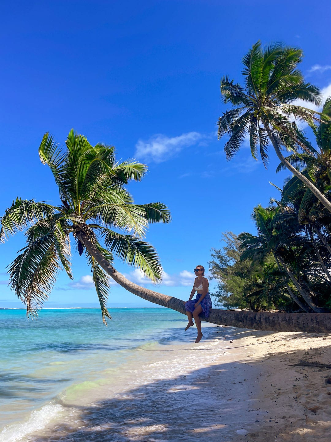Scenic tropical beach with palm trees and a person relaxing by the sea. Bent palm tree behind Charlie's Raro