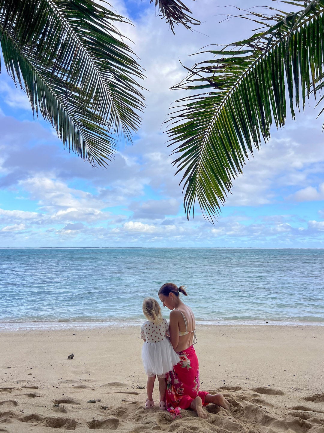 Mother and daughter on the beach under palm trees with ocean view in Rarotonga